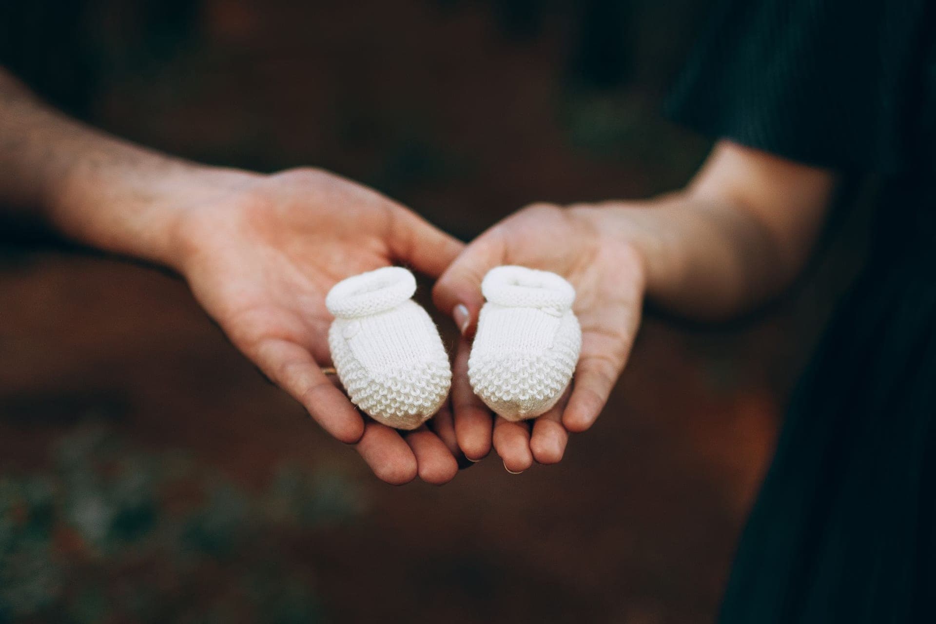 Two pairs of hands holding a small pair of knitted baby booties